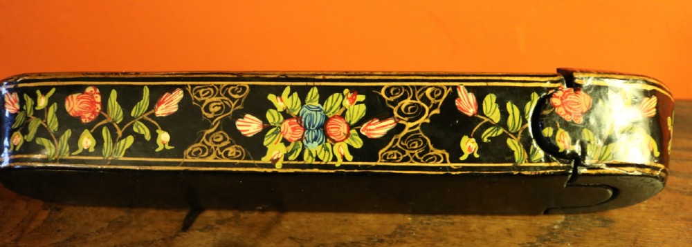 An elongated, rounded antique Indo-Persian lacquered papier-mache pen case featuring hand-painted figures in a landscape with floral end caps. View V