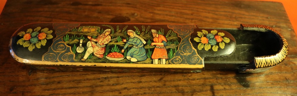 An elongated, rounded antique Indo-Persian lacquered papier-mache pen case featuring hand-painted figures in a landscape with floral end caps. View VII