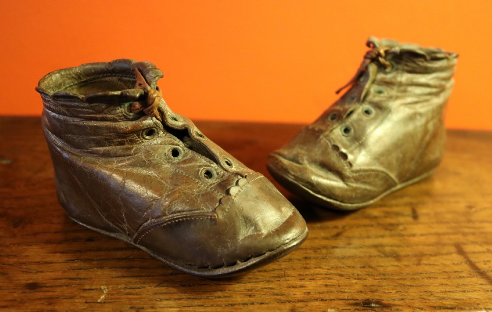 A pair of aged dark brown leather Victorian childrens ankle boots featuring laced fronts with metal eyelets.