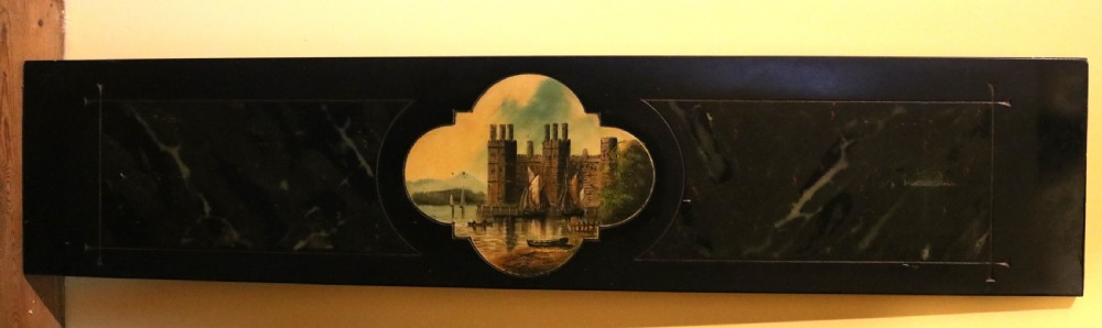 A long rectangular black slate panel featuring a central painted vignette of Caernarfon Castle within a quatrefoil border and faux-marbled side sections.