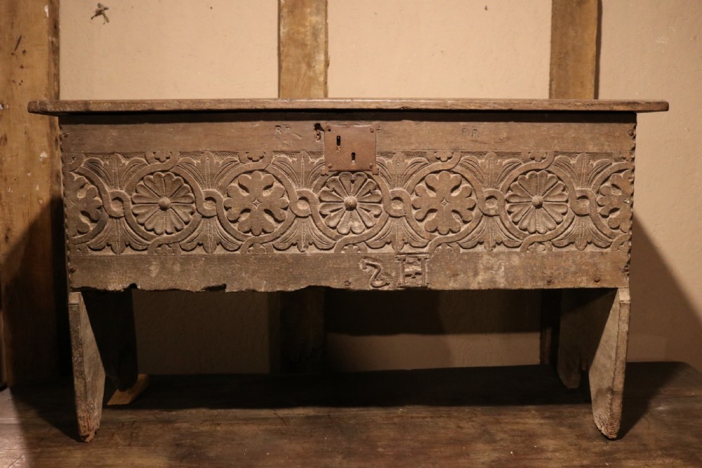 A 16th-century Tudor carved oak coffer featuring a carved rosette frieze, central wrought iron lockplate, and slab end supports.