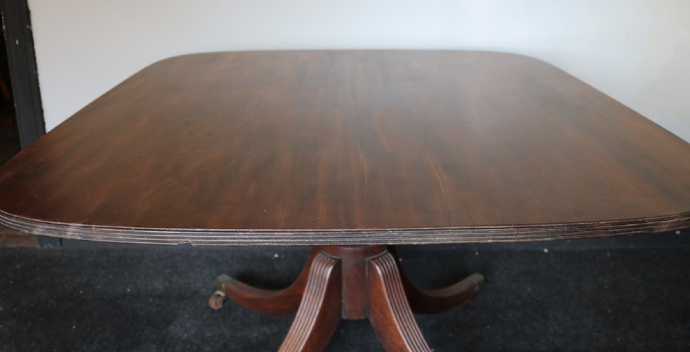A Regency mahogany breakfast table featuring a rectangular top with reeded edges, a turned central pedestal, and four splayed reeded legs on brass castors. View VI