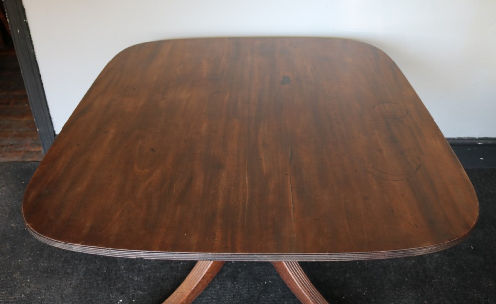 A Regency mahogany breakfast table featuring a rectangular top with reeded edges, a turned central pedestal, and four splayed reeded legs on brass castors. View VII