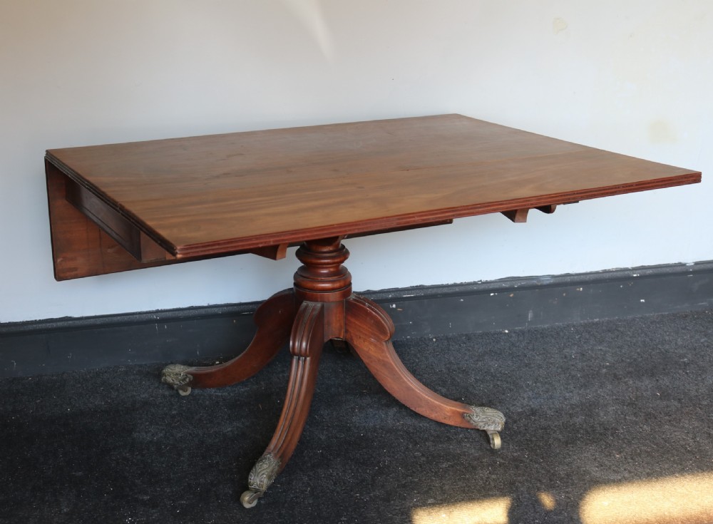 A Regency mahogany dining table featuring a rectangular drop-leaf top supported by a central reeded pedestal and four splayed legs with brass toe castors. View III