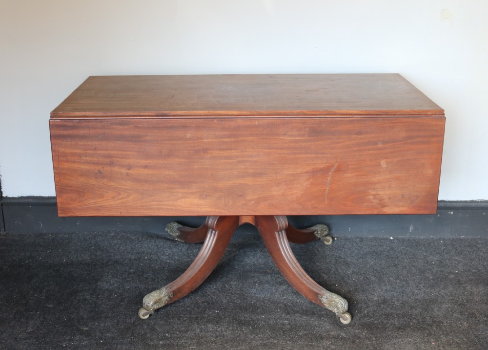 A Regency mahogany dining table featuring a rectangular drop-leaf top supported by a central reeded pedestal and four splayed legs with brass toe castors. View V