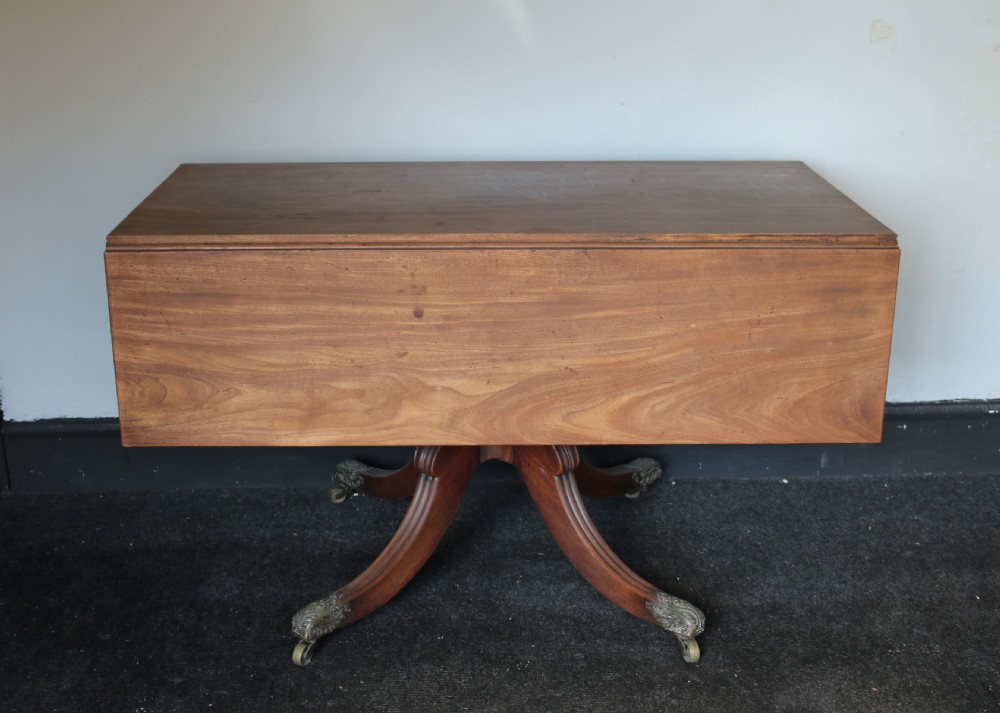 A Regency mahogany dining table featuring a rectangular drop-leaf top supported by a central reeded pedestal and four splayed legs with brass toe castors. View VI