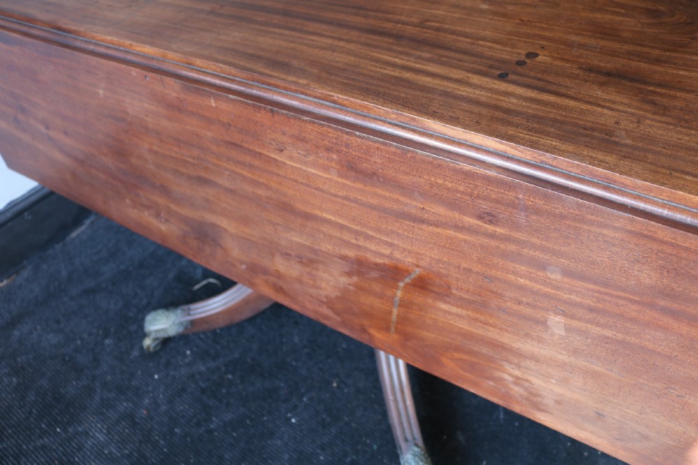 A Regency mahogany dining table featuring a rectangular drop-leaf top supported by a central reeded pedestal and four splayed legs with brass toe castors. View XI