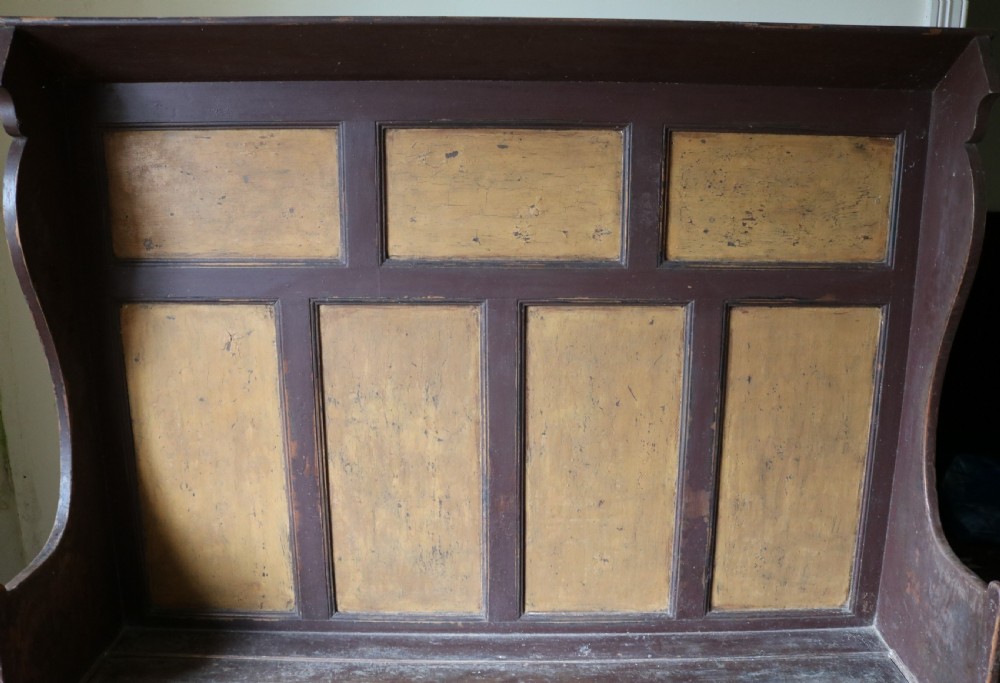 A high-backed Welsh pine settle bench featuring a two-tone dark brown and ochre painted finish with raised panel detailing and shaped wing sides. View IX
