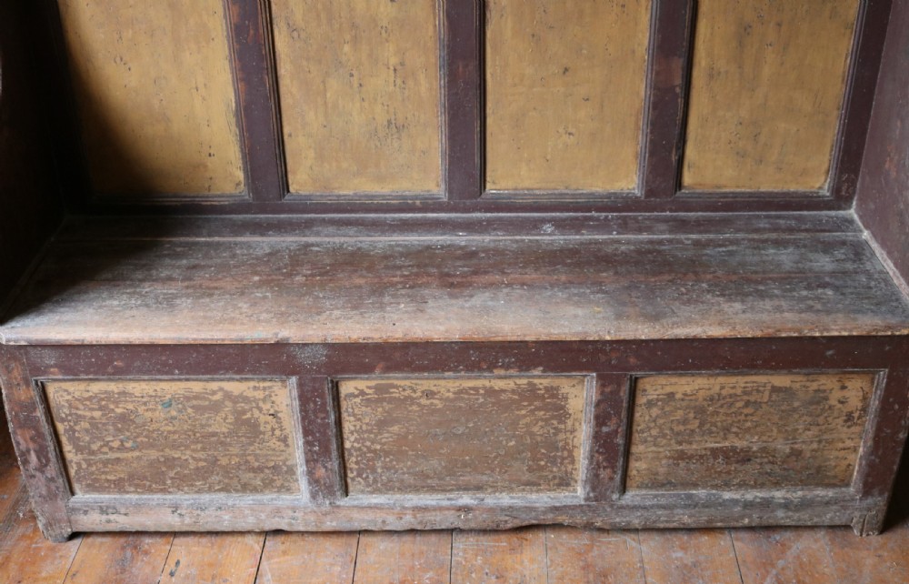 A high-backed Welsh pine settle bench featuring a two-tone dark brown and ochre painted finish with raised panel detailing and shaped wing sides. View X