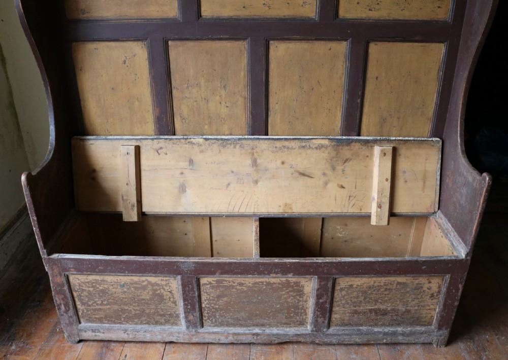 A high-backed Welsh pine settle bench featuring a two-tone dark brown and ochre painted finish with raised panel detailing and shaped wing sides. View XVI