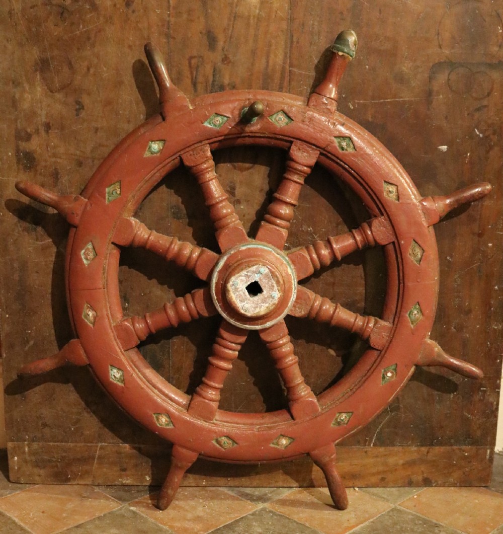 A nineteenth-century Welsh wooden ships wheel finished in deep red paint with turned spokes and green diamond motifs along the outer rim.