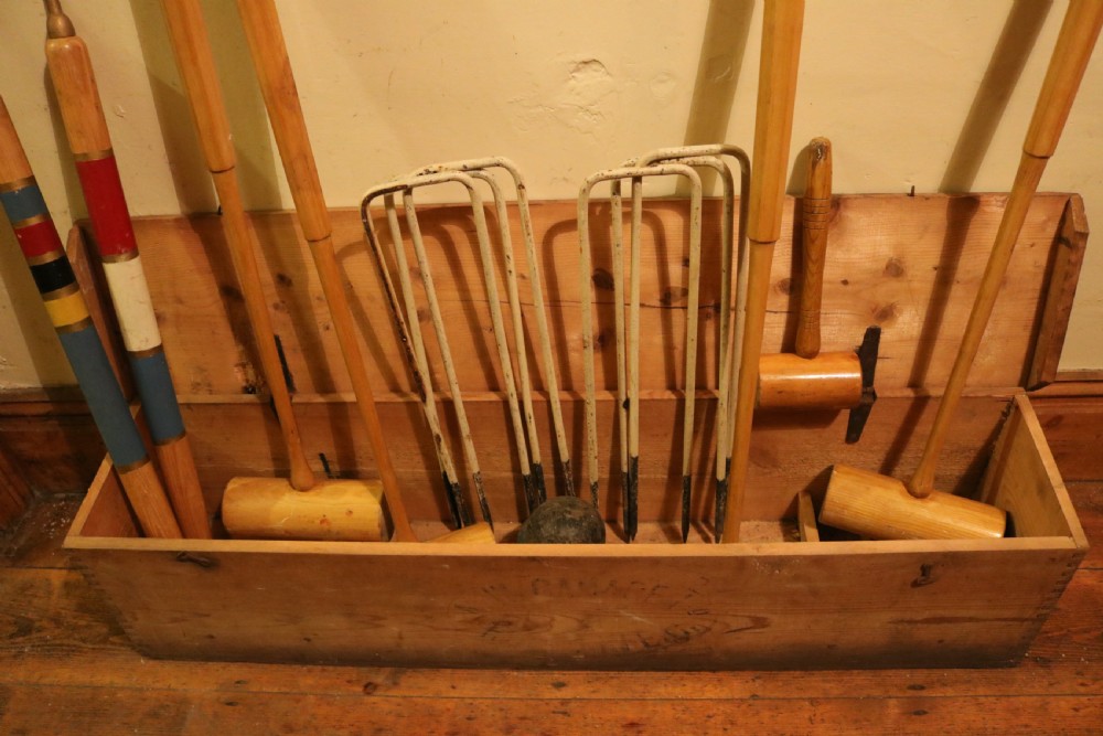 An open pine box containing an antique croquet set with wooden mallets, painted winning posts, and white metal hoops. View II