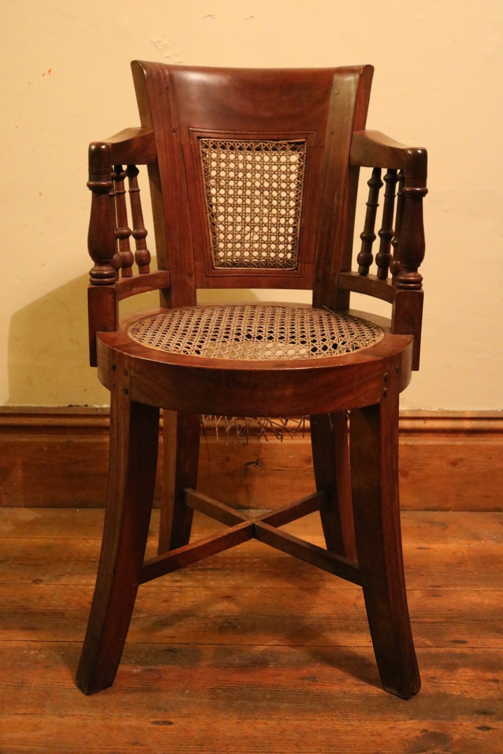 A Victorian mahogany parlour chair featuring a woven cane seat, curved backrest, and turned spindle armrests.