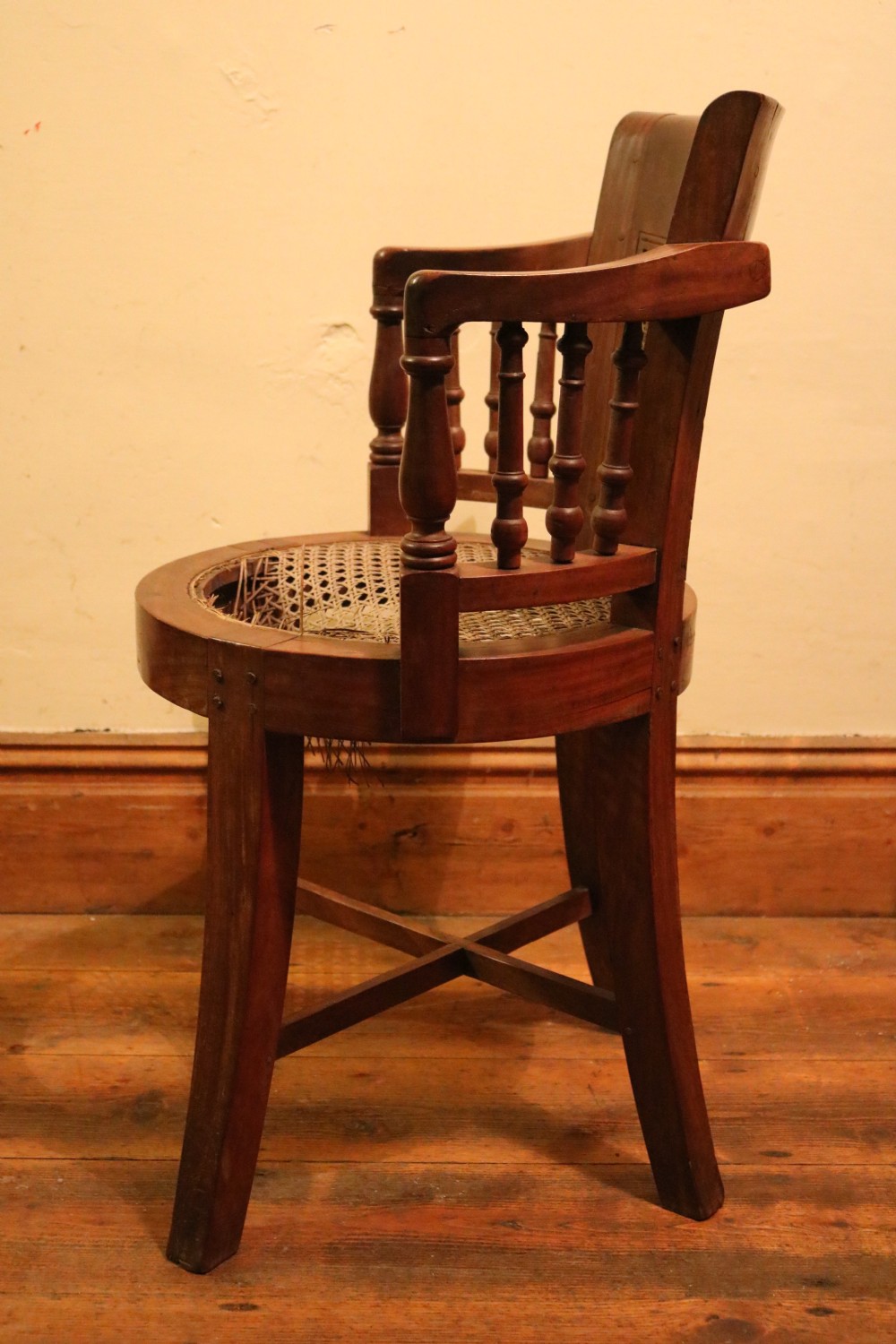 A Victorian mahogany parlour chair featuring a woven cane seat, curved backrest, and turned spindle armrests. View VI