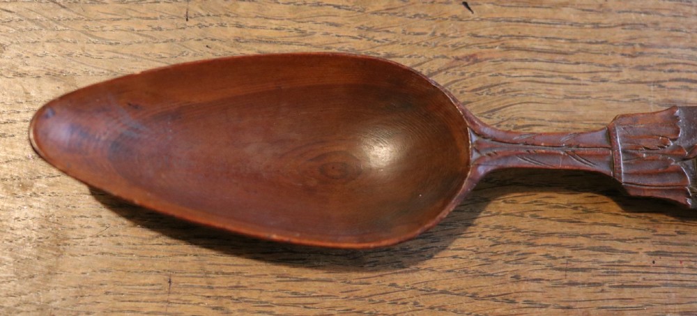 A hand-carved dark yew-wood spoon featuring a detailed relief design of grapevines and fruit along its flat handle. View II