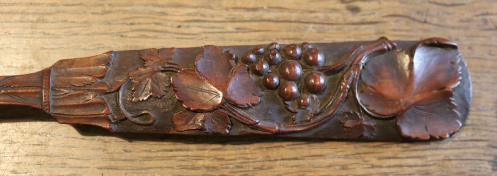 A hand-carved dark yew-wood spoon featuring a detailed relief design of grapevines and fruit along its flat handle. View III