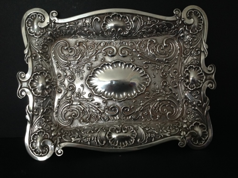 An Edwardian sterling silver rectangular dressing table tray featuring embossed floral scrollwork repousse decoration and a fluted oval centre cartouche.