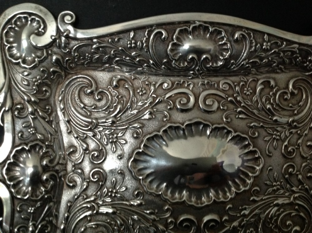 An Edwardian sterling silver rectangular dressing table tray featuring embossed floral scrollwork repousse decoration and a fluted oval centre cartouche. View II
