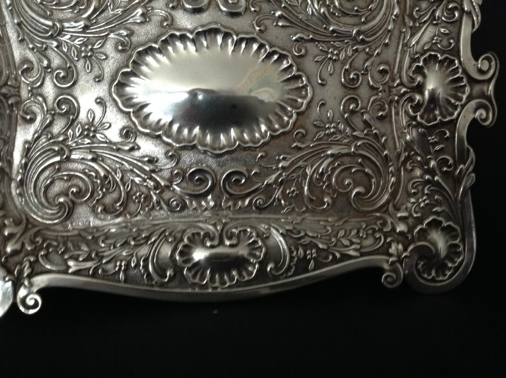 An Edwardian sterling silver rectangular dressing table tray featuring embossed floral scrollwork repousse decoration and a fluted oval centre cartouche. View III