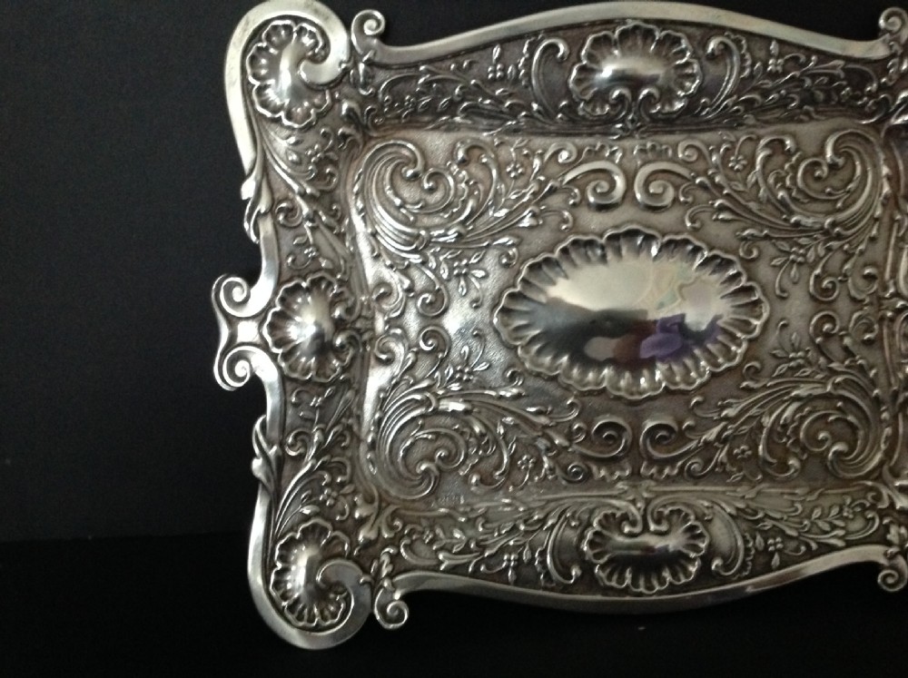 An Edwardian sterling silver rectangular dressing table tray featuring embossed floral scrollwork repousse decoration and a fluted oval centre cartouche. View IV