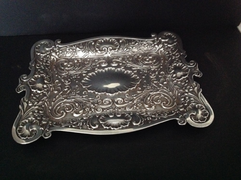 An Edwardian sterling silver rectangular dressing table tray featuring embossed floral scrollwork repousse decoration and a fluted oval centre cartouche. View V
