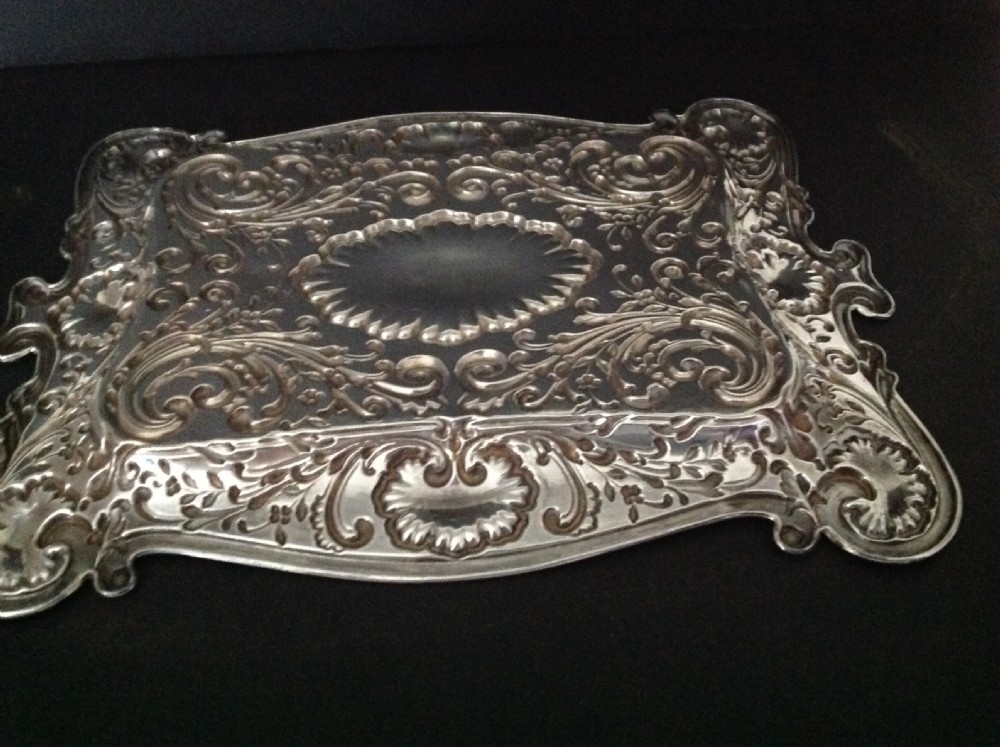 An Edwardian sterling silver rectangular dressing table tray featuring embossed floral scrollwork repousse decoration and a fluted oval centre cartouche. View VI