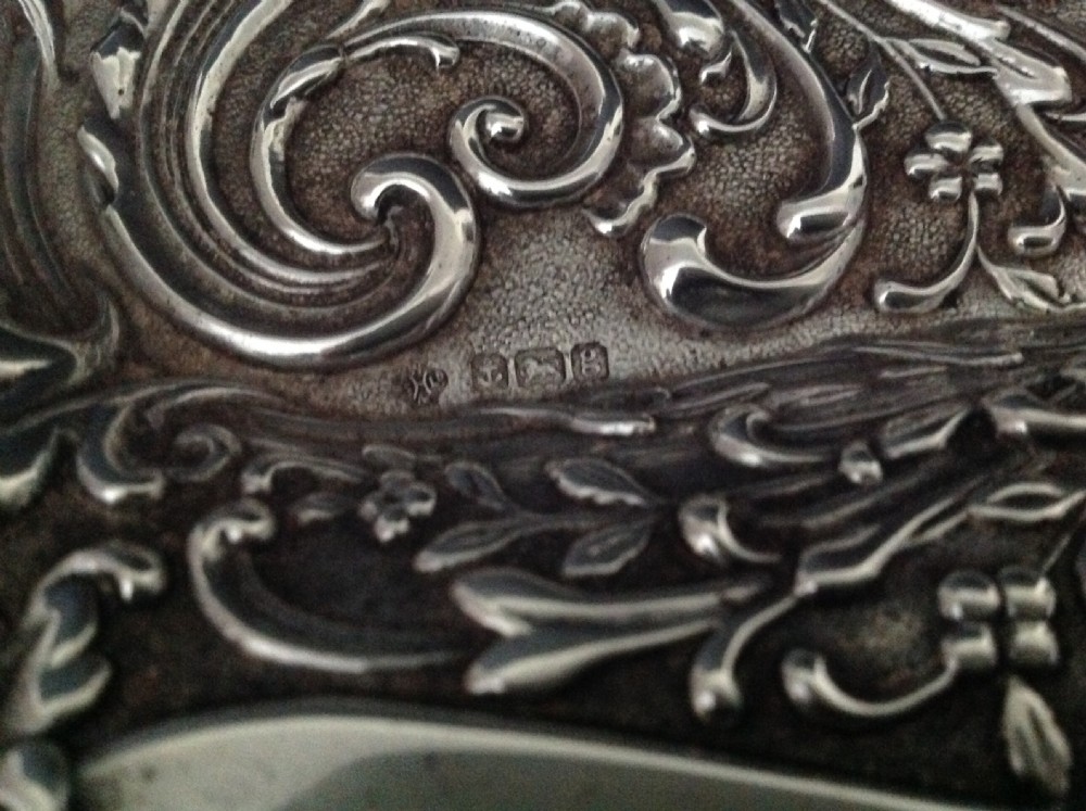 An Edwardian sterling silver rectangular dressing table tray featuring embossed floral scrollwork repousse decoration and a fluted oval centre cartouche. View VII