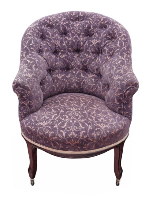fig 2. An antique Victorian tub armchair upholstered in patterned dusty purple fabric with a button-tufted backrest and mahogany legs on brass castors.