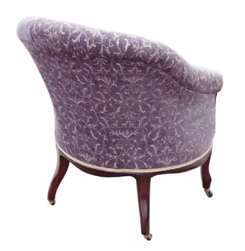 fig 3. An antique Victorian tub armchair upholstered in patterned dusty purple fabric with a button-tufted backrest and mahogany legs on brass castors.