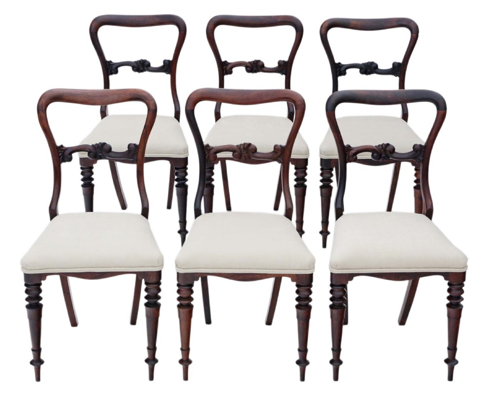 A set of six Victorian rosewood balloon back dining chairs featuring carved central splats, turned front legs, and cream upholstered seats.