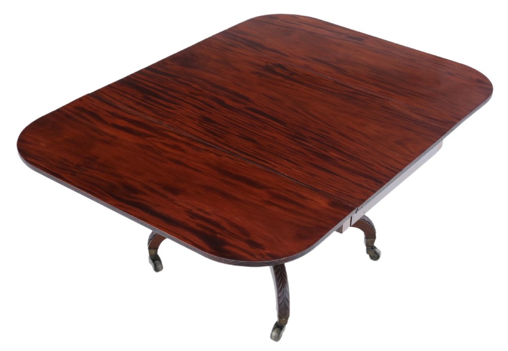 A Regency period Cuban mahogany drop leaf dining table extended with a central pedestal and four reeded splayed legs on brass castors. View IV
