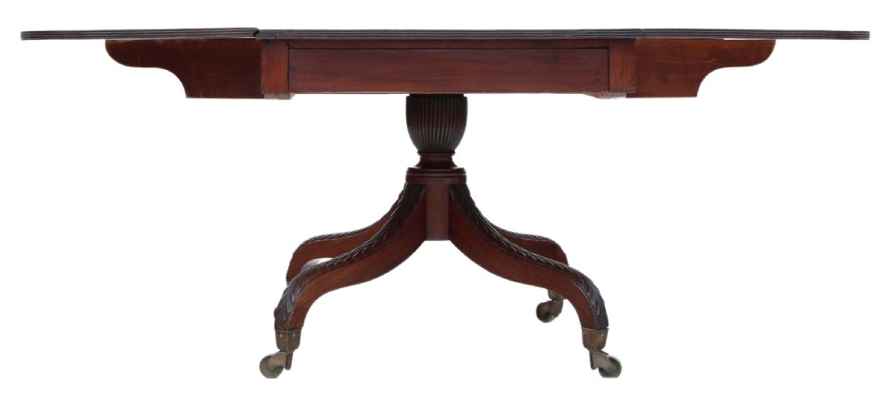 A Regency period Cuban mahogany drop leaf dining table extended with a central pedestal and four reeded splayed legs on brass castors. View V