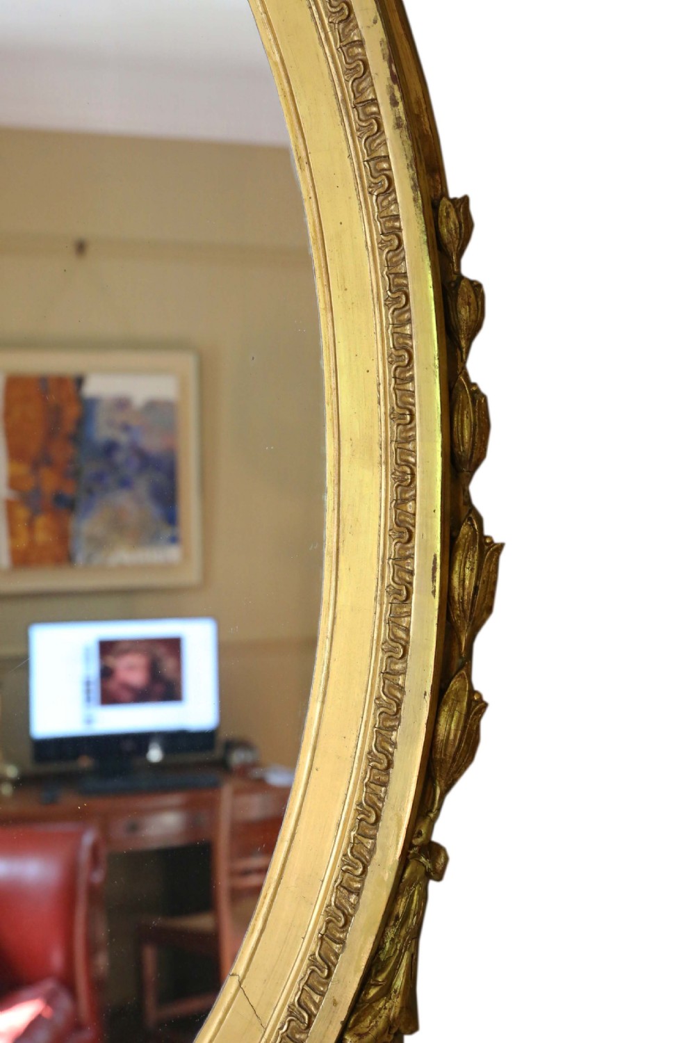 An antique gold gilt oval wall mirror featuring a Neoclassical ribbon motif at the base and foliage side supports. View II