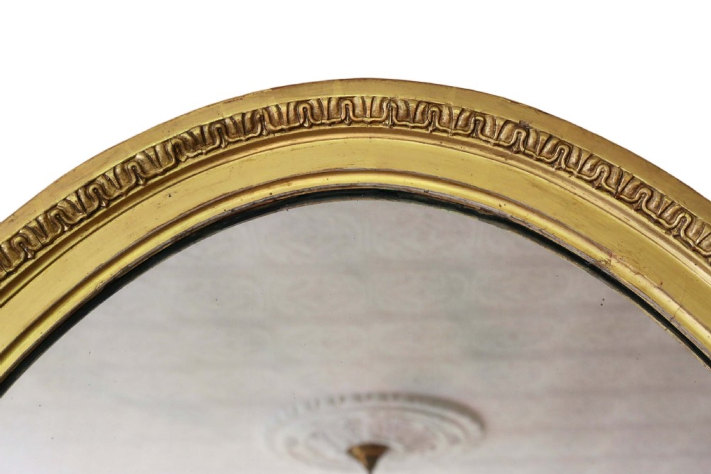 An antique gold gilt oval wall mirror featuring a Neoclassical ribbon motif at the base and foliage side supports. View III