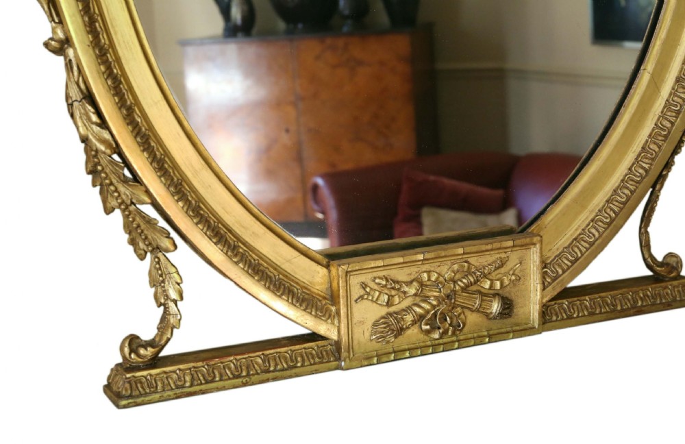 An antique gold gilt oval wall mirror featuring a Neoclassical ribbon motif at the base and foliage side supports. View IV