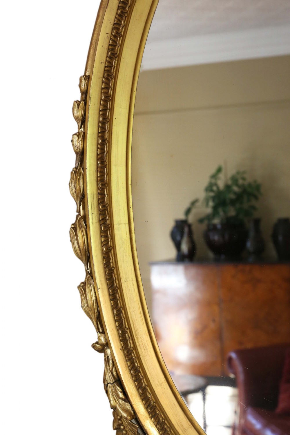 An antique gold gilt oval wall mirror featuring a Neoclassical ribbon motif at the base and foliage side supports. View V