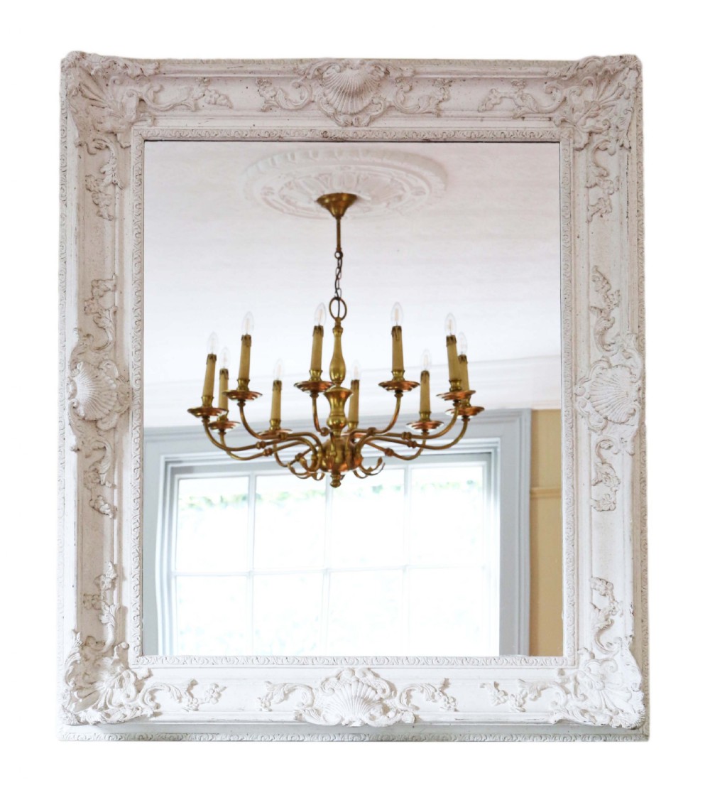 A large rectangular overmantel mirror featuring an off-white carved gesso frame decorated with scallop shell motifs, foliage, and corner crests.