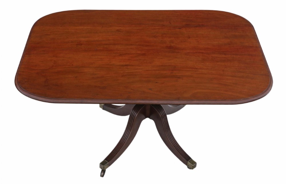 A Regency mahogany tilt-top loo table shown in a tilted position with a central pedestal and four reeded legs fitted with brass castors. View IV