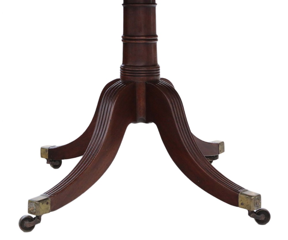 A Regency mahogany tilt-top loo table shown in a tilted position with a central pedestal and four reeded legs fitted with brass castors. View V