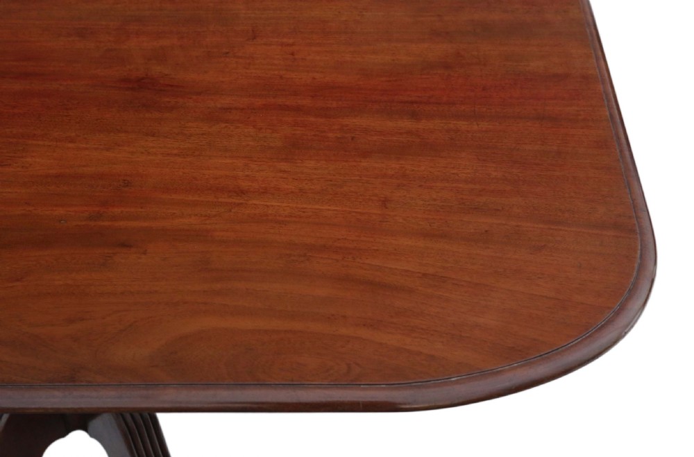 A Regency mahogany tilt-top loo table shown in a tilted position with a central pedestal and four reeded legs fitted with brass castors. View VII