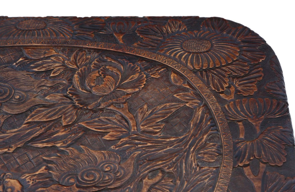 A dark carved hardwood table featuring detailed relief carvings of floral patterns on the top, curved cabriole legs, and an X-shaped stretcher. View IV