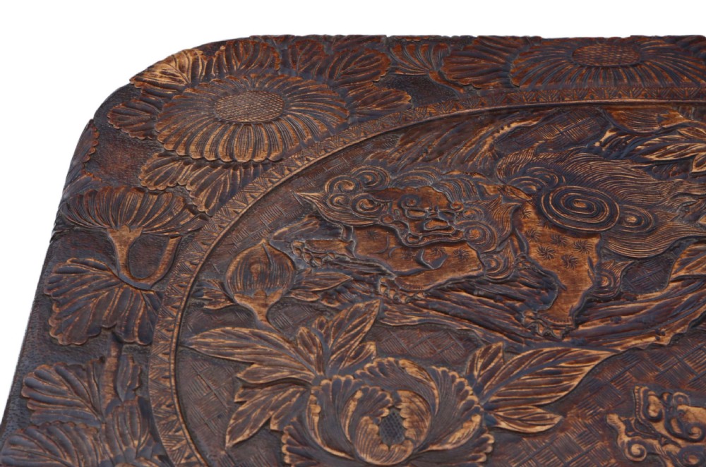 A dark carved hardwood table featuring detailed relief carvings of floral patterns on the top, curved cabriole legs, and an X-shaped stretcher. View V