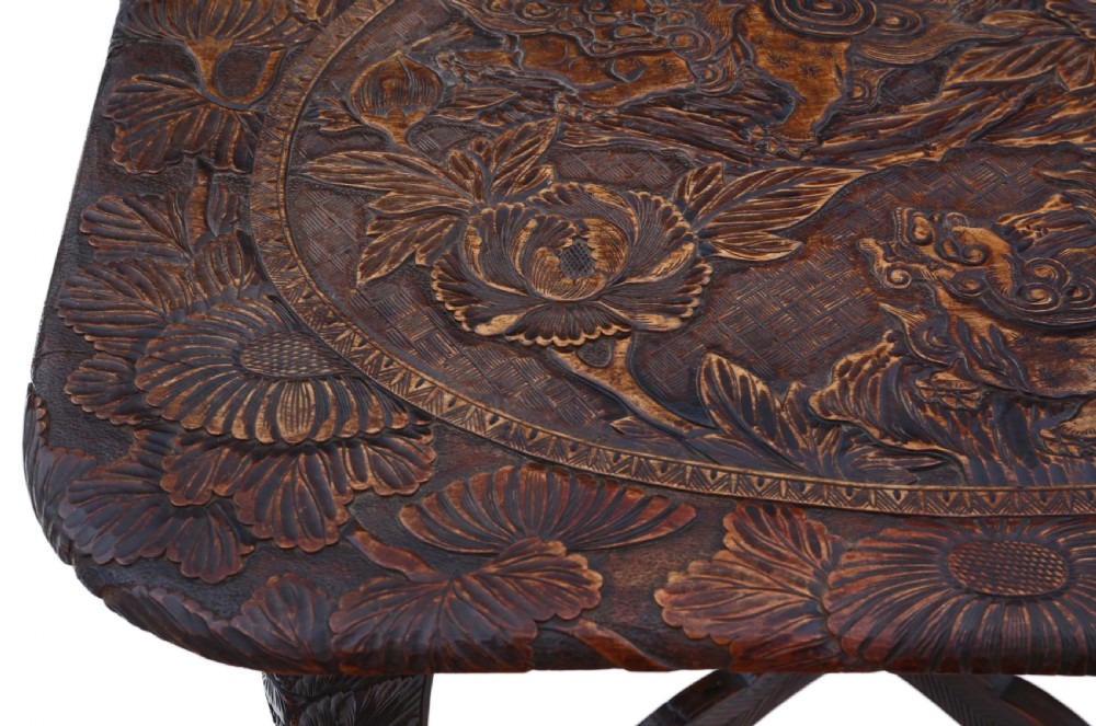 A dark carved hardwood table featuring detailed relief carvings of floral patterns on the top, curved cabriole legs, and an X-shaped stretcher. View VI
