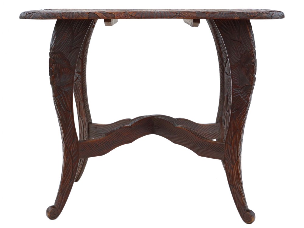 A dark carved hardwood table featuring detailed relief carvings of floral patterns on the top, curved cabriole legs, and an X-shaped stretcher. View VII