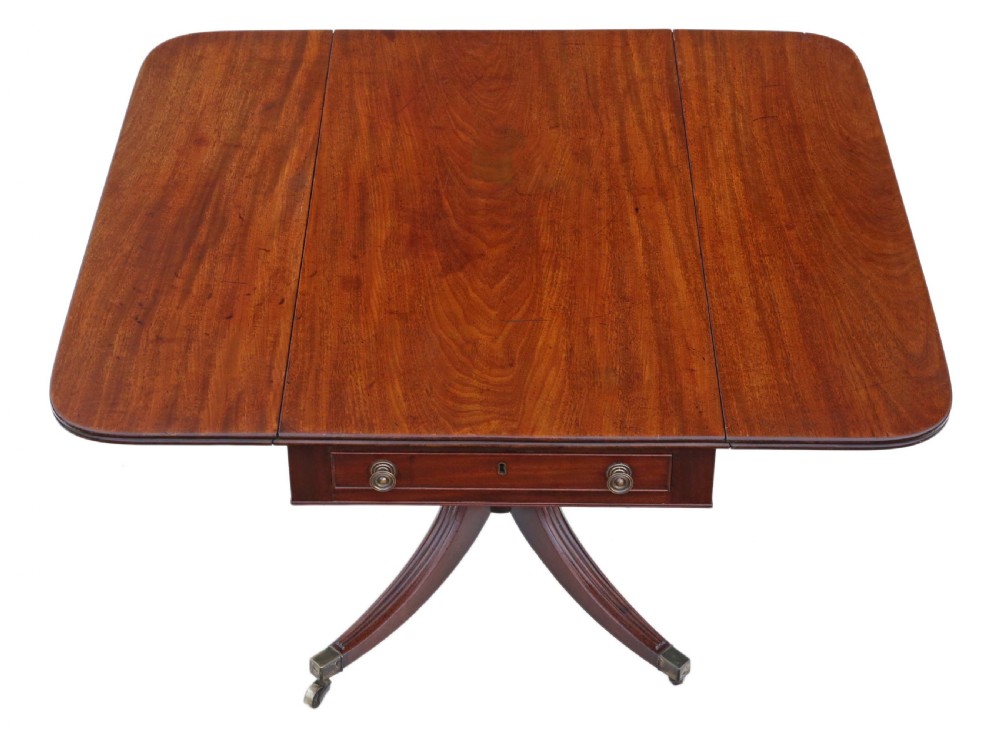 A Regency mahogany drop-leaf table featuring two hinged rectangular leaves, a single frieze drawer with brass handles, and a pedestal base with four reeded splayed legs fitted with brass castors.