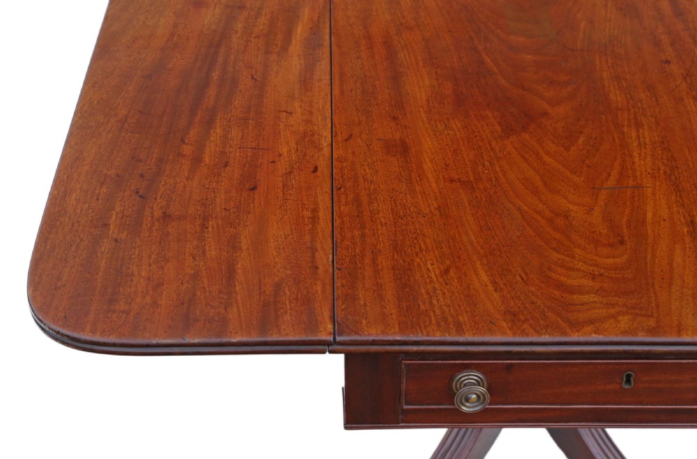 A Regency mahogany drop-leaf table featuring two hinged rectangular leaves, a single frieze drawer with brass handles, and a pedestal base with four reeded splayed legs fitted with brass castors. View II