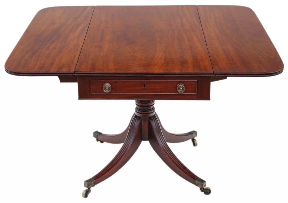 A Regency mahogany drop-leaf table featuring two hinged rectangular leaves, a single frieze drawer with brass handles, and a pedestal base with four reeded splayed legs fitted with brass castors. View V