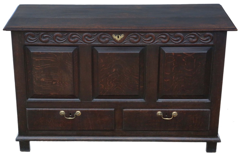 A dark oak Georgian mule chest featuring a carved wave frieze, three fielded front panels, two base drawers with brass handles, and square feet.