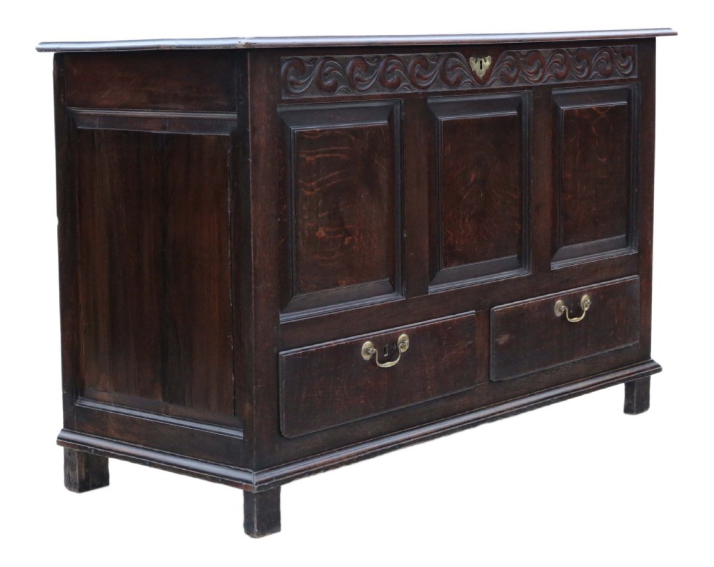 A dark oak Georgian mule chest featuring a carved wave frieze, three fielded front panels, two base drawers with brass handles, and square feet. View VI