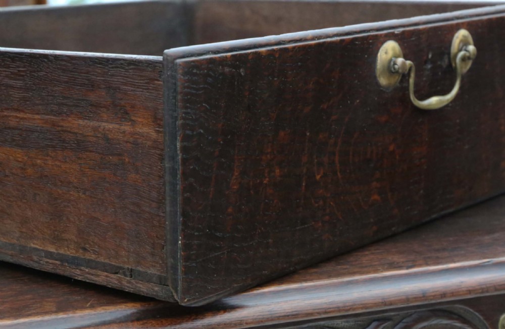 A dark oak Georgian mule chest featuring a carved wave frieze, three fielded front panels, two base drawers with brass handles, and square feet. View VII